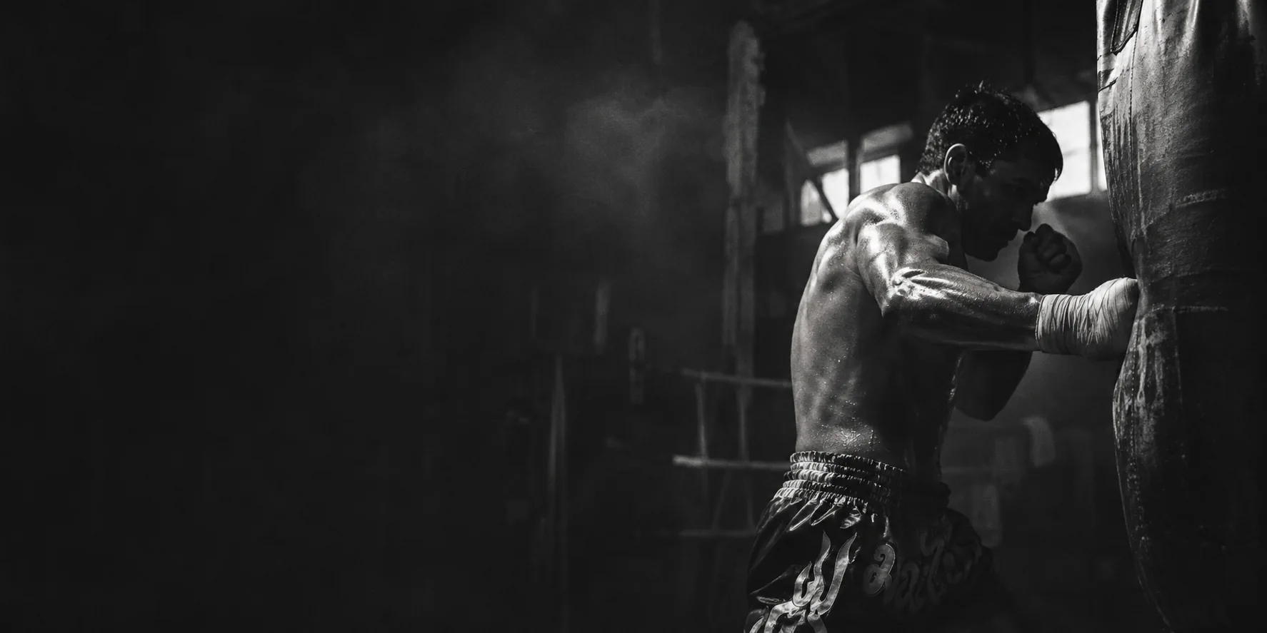 Black-and-white illustrative photograph of a fighter striking a heavy bag